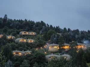 An evening view of the Bisate Lodge. Bisate Lodge is located in the natural amphitheatre of an eroded volcanic cone – the word bisate means ‘pieces’ in Kinyarwanda, describing how the cone was once whole but worn away by natural erosion. The lodge is built on a hill in front of the volcanoes Bisoke, Karisimbi and Mikeno rearing up through the Afro-alpine forests of nearby Volcanoes National Park. © Andrea Frazzetta / INSTITUTE